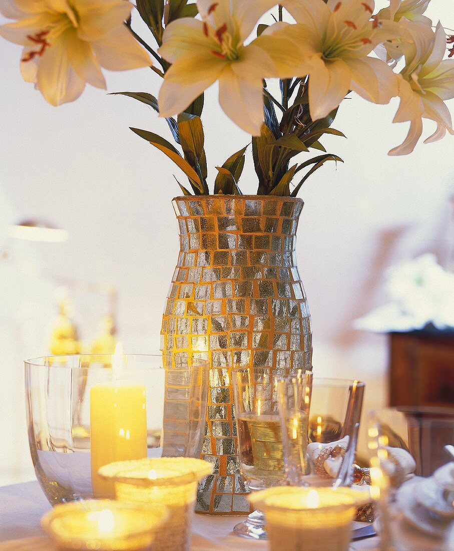 weiße Lilien in Glasmosaikvase und Teelichter