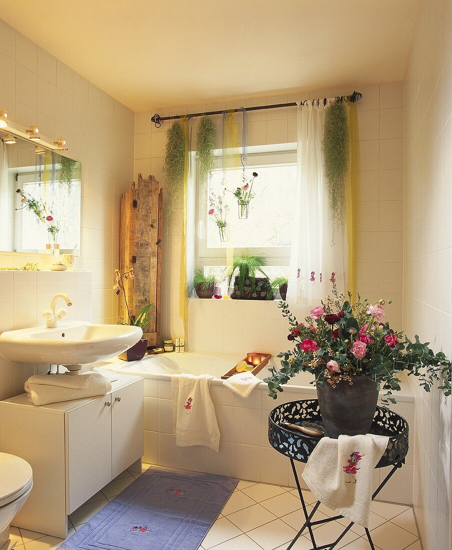 Blick in ein Bad mit Blumengesteck auf Tablett-Tisch und Pflanzendekoration am Fenster