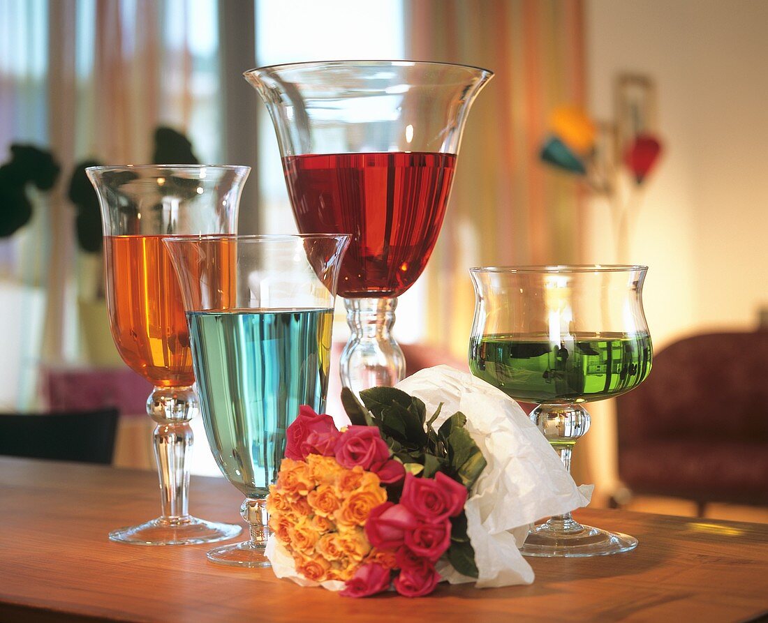 Glasses of coloured water and bouquet of roses, lying