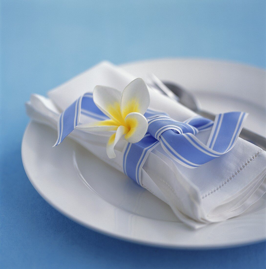 Place-setting with white fabric napkin, flower & blue bow