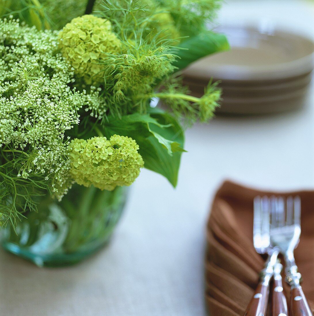 Posy of green flowers beside brown napkins and forks