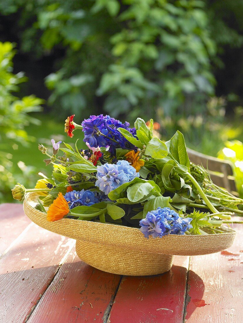 Sommerblumen in einem Strohhut auf Gartentisch