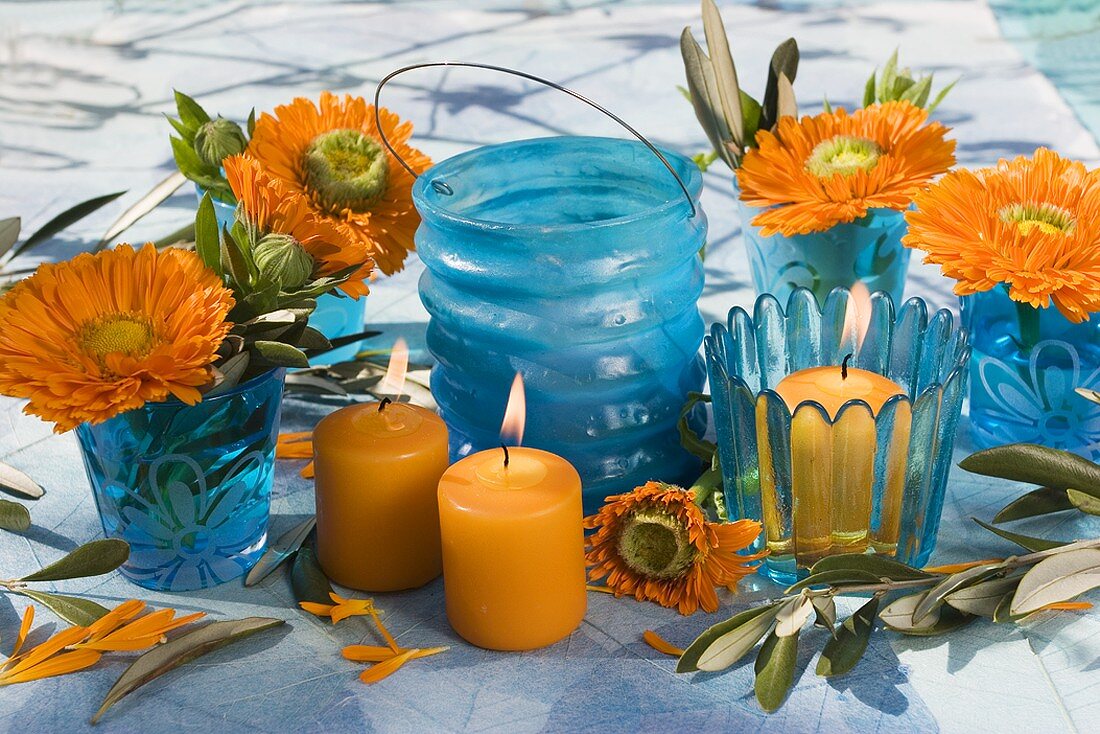 Marigolds and olive sprigs in blue glasses, candles