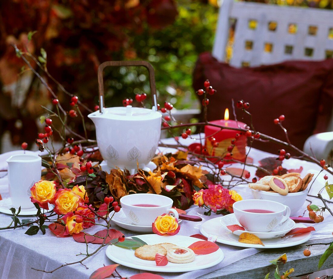 Teetisch mit Rosen, Hagebutten und Kranz aus Herbstlaub