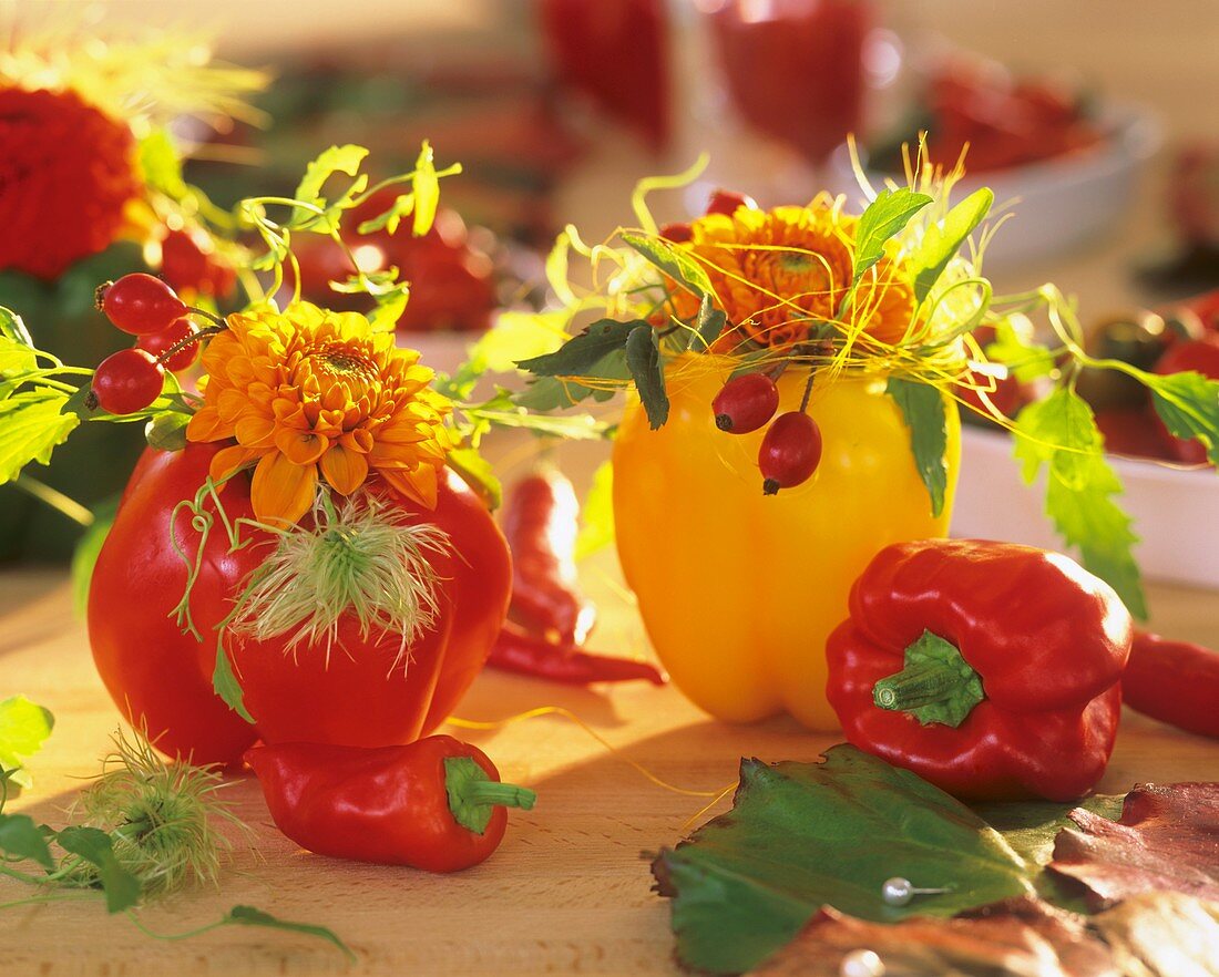 Rote und gelbe Paprika als Vase mit Dahlien und Hagebutten