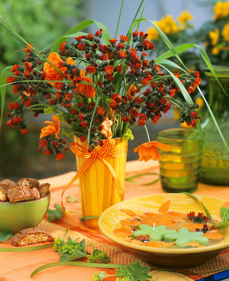Vase of hawkweed; bowl with floating candles; biscotti