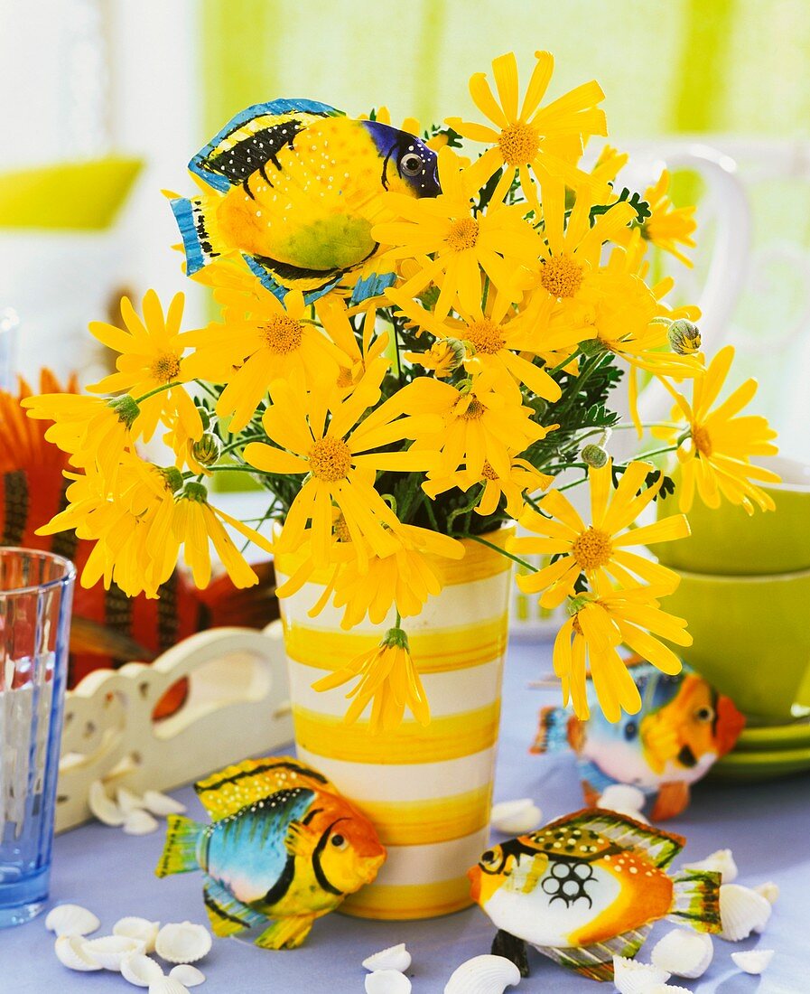 Vase of yellow marguerites, fish and shells