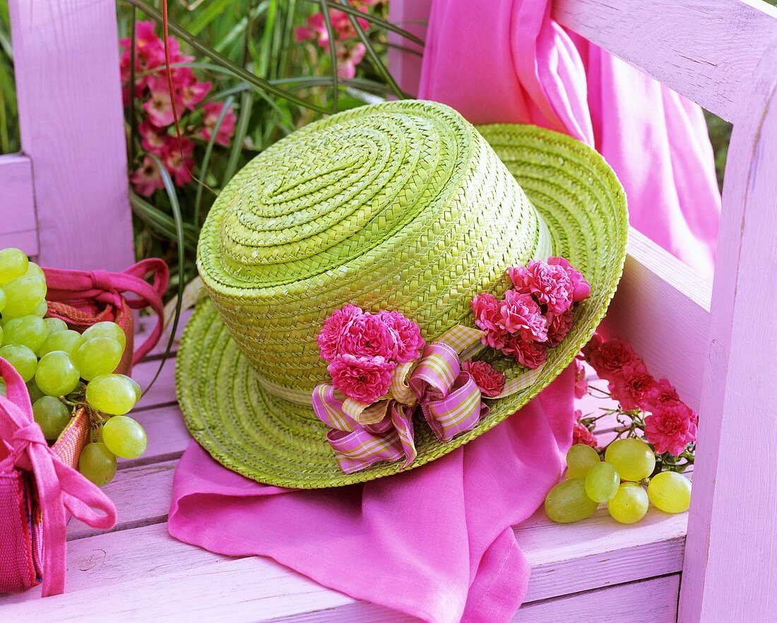 Green straw hat with roses on pink bench, grapes