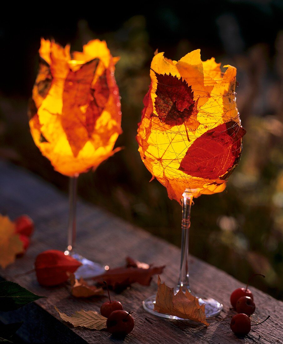 Weingläser mit Teelichtern, umwickelt mit buntem Herbstlaub