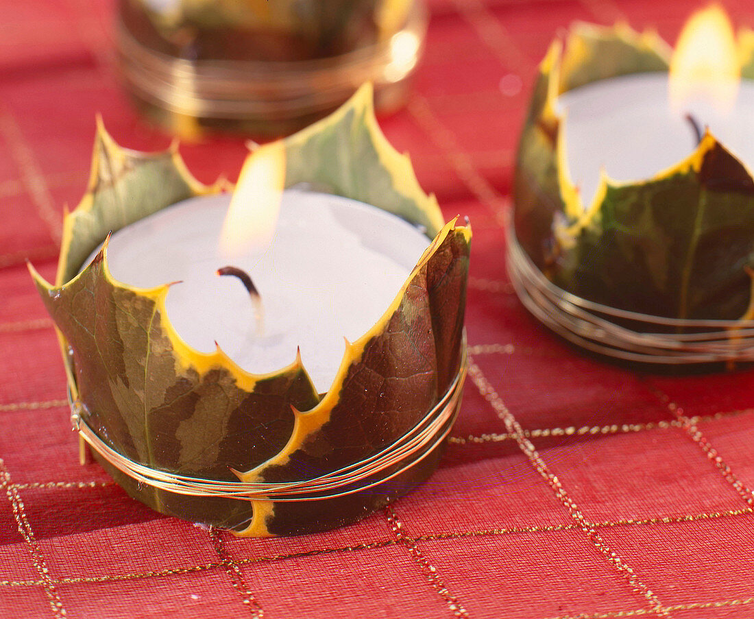 Tea lights decorated with holly leaves as table decorations