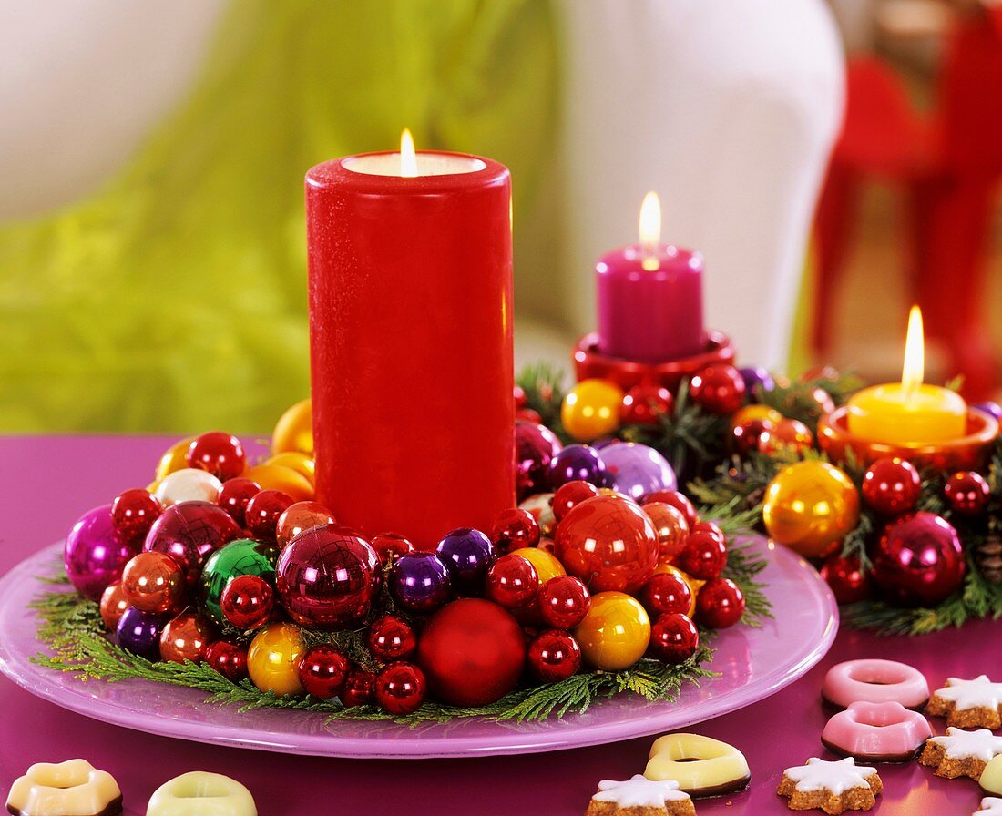 Red candle in wreath of false cypress and coloured baubles