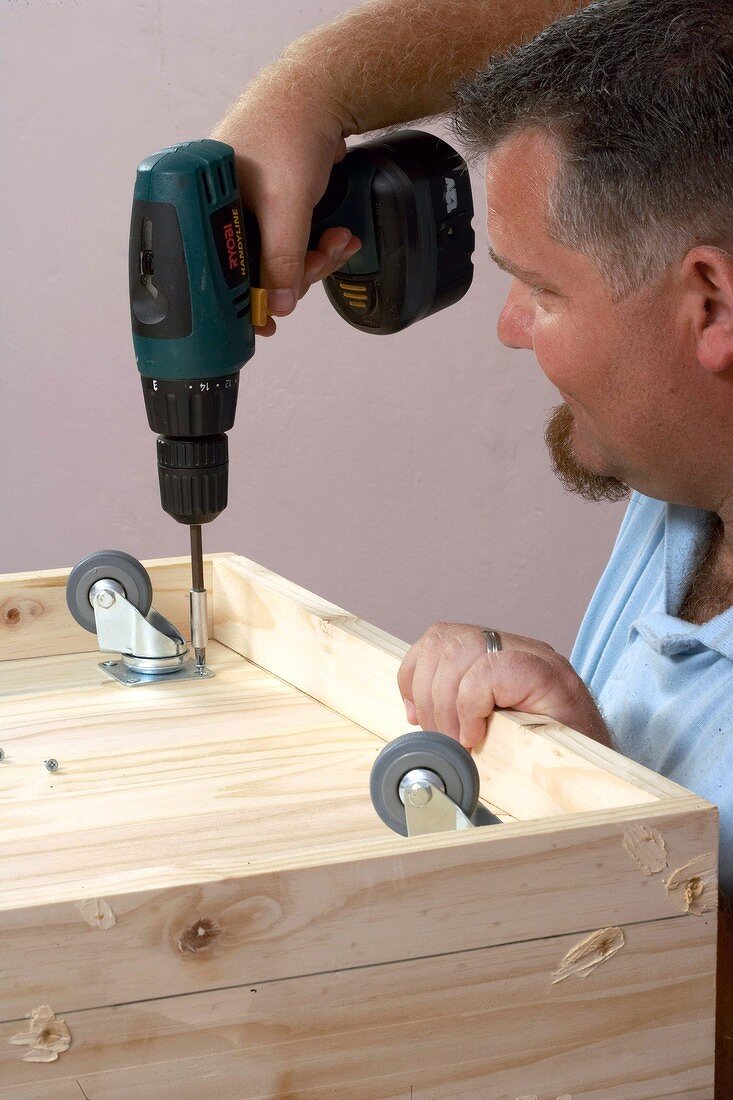 Man screwing casters on to a piece of wooden furniture