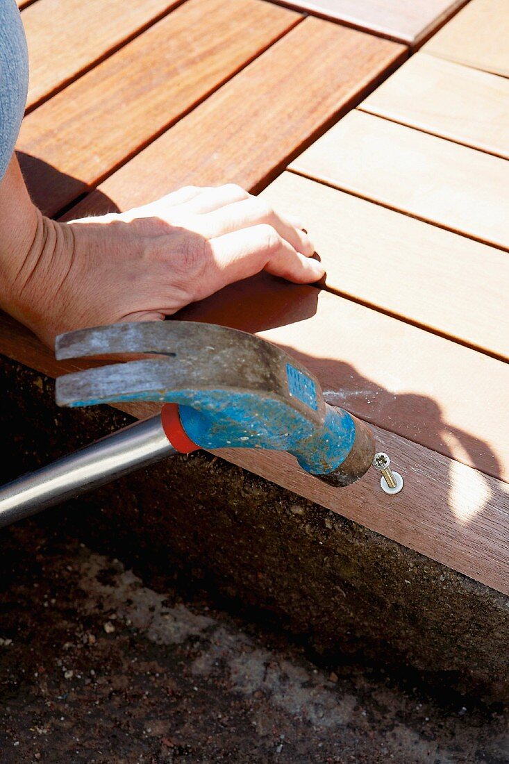 Woman hammering screw into wooden edging