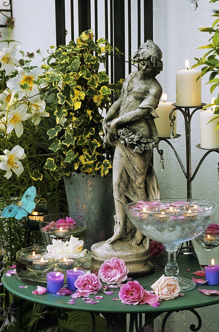 Tisch mit Kerzen, Rosenblüten und Steinfigur auf der Terrasse