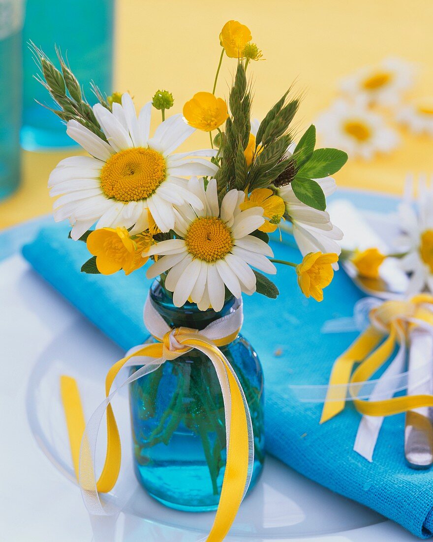 Posy of marguerites and buttercups in turquoise bottle