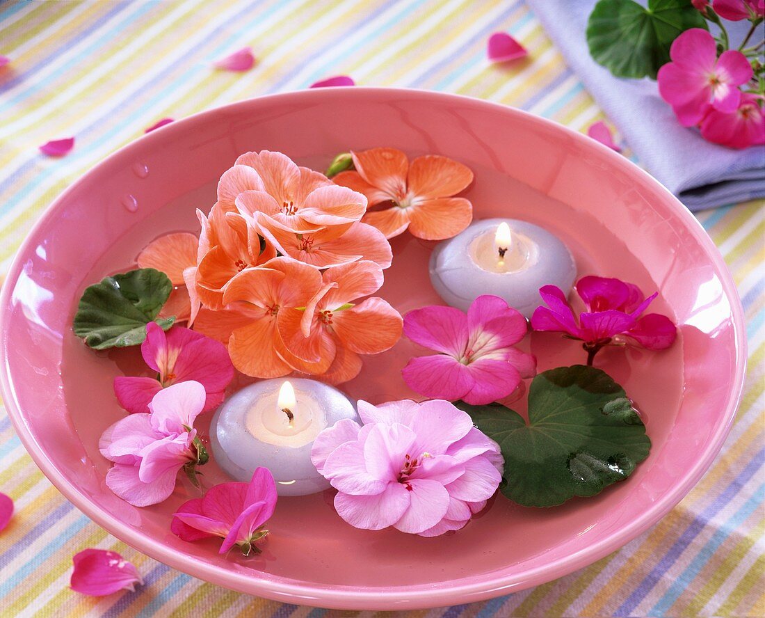 Geranium flowers and leaves and floating candles in bowl