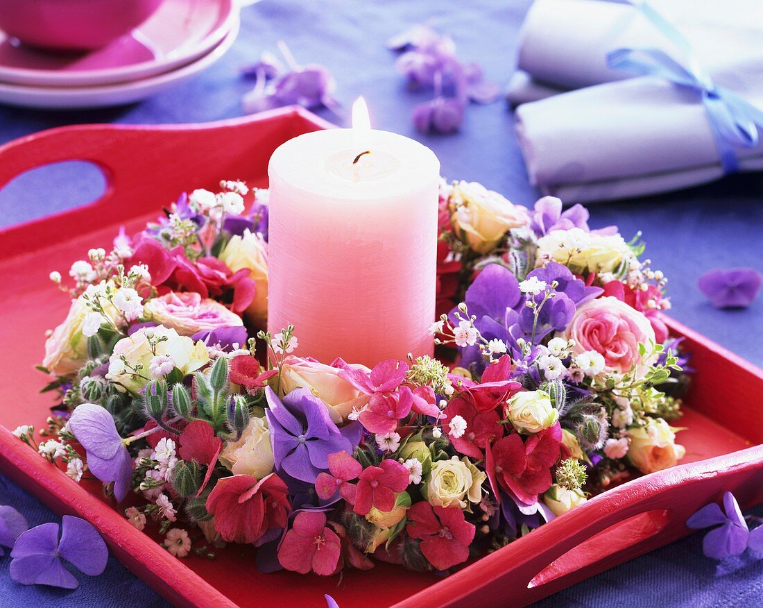 Blütenkranz um rosa Kerze auf einem Tablett