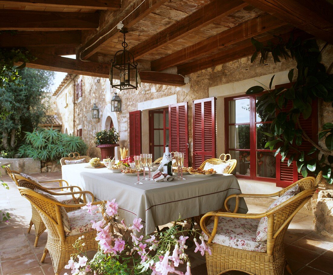 A table laid with appetizers and sparkling wine on a covered patio of an old, French country house