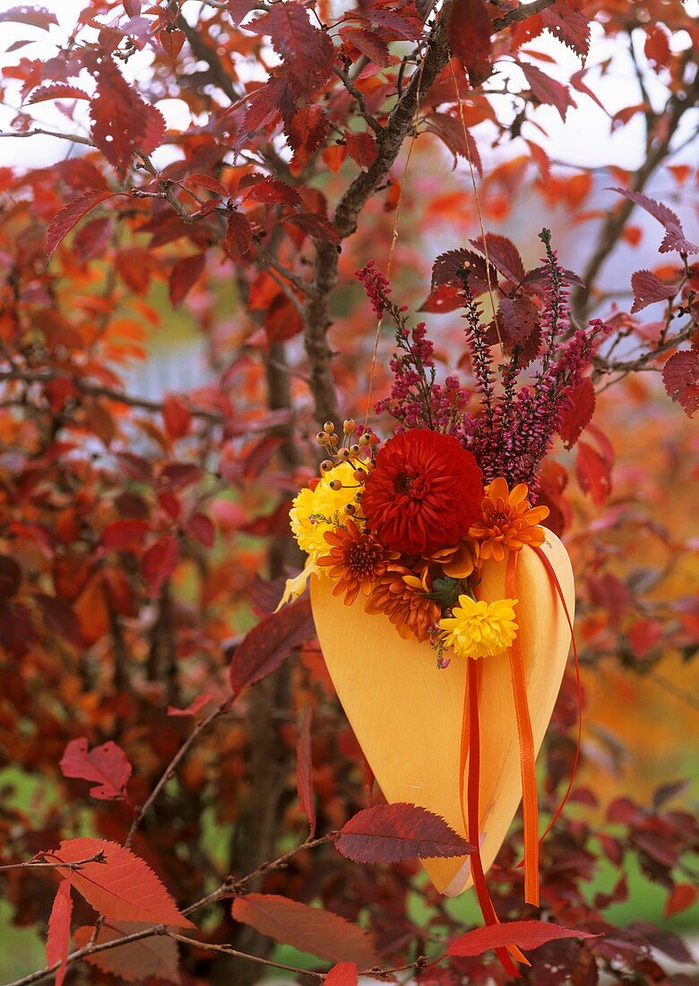 Gelbe Vase mit Herbstblumen an Zweig gehängt