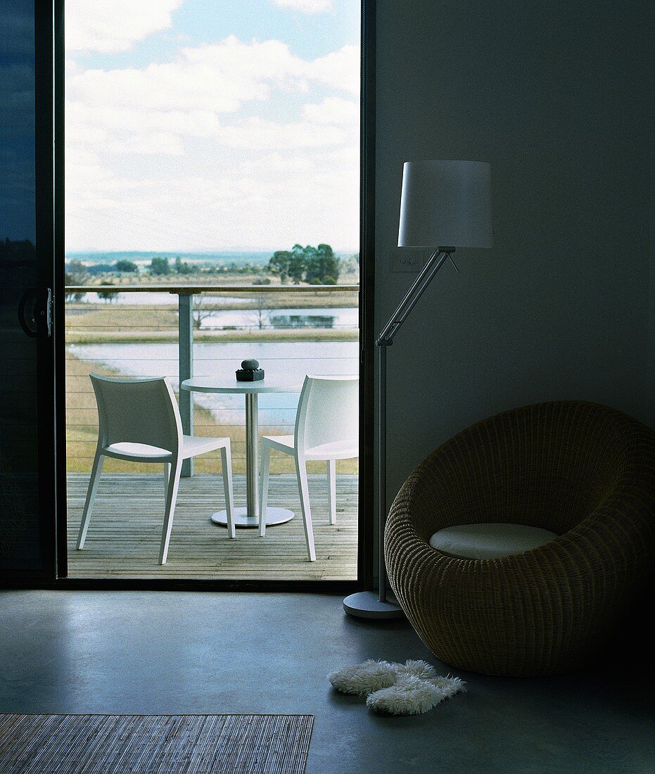 Runder Korbstuhl in Hotelzimmer mit puristischer Holzterrasse und Blick in die weite Landschaft