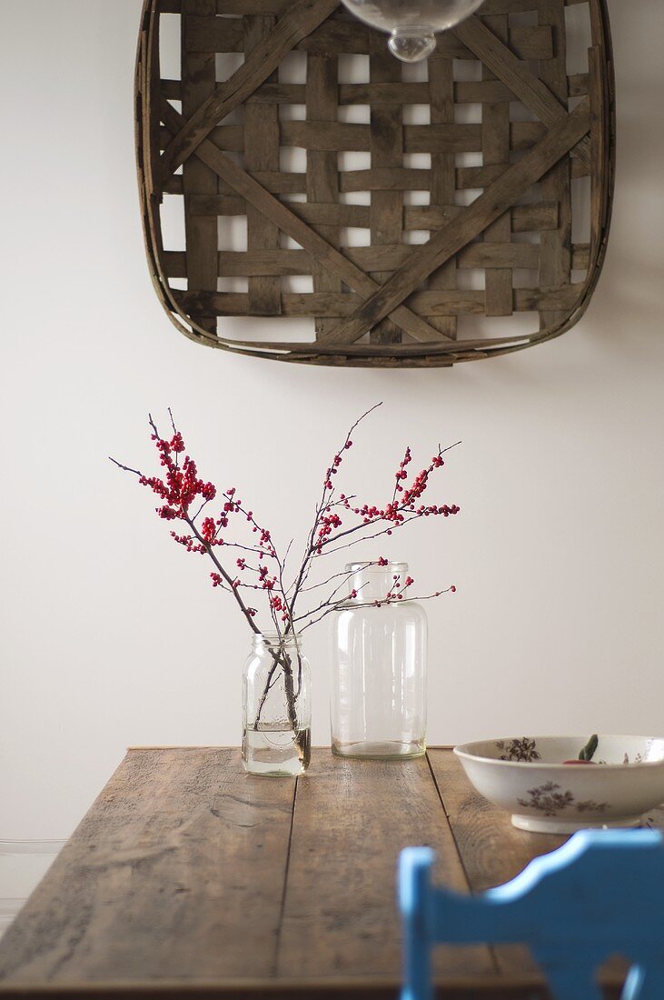 Woven basket on wall above twigs in glass jar on rustic wooden table
