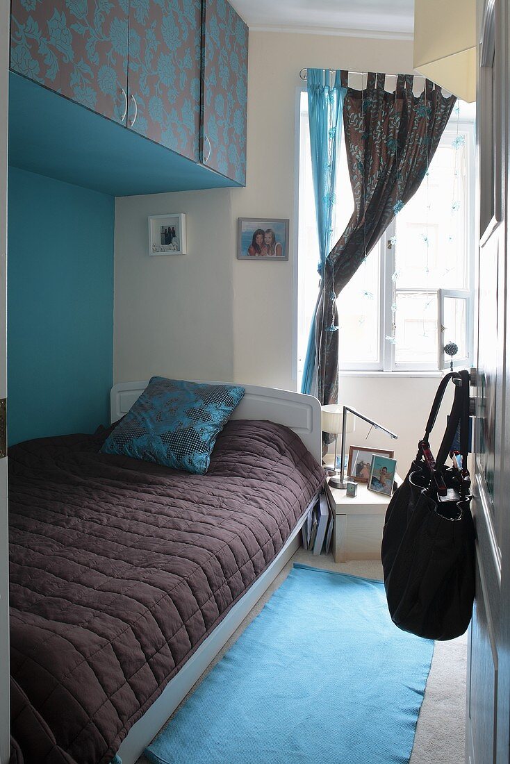 View into colour-coordinated bedroom with single bed below wall-mounted cupboards