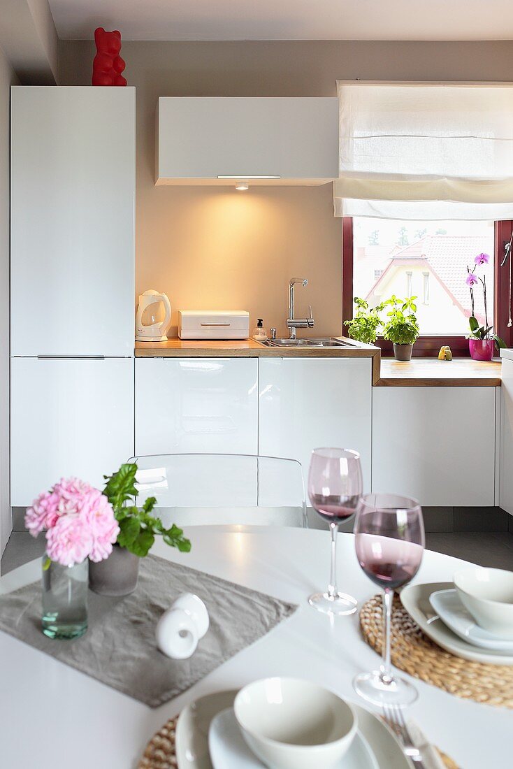Gedeckter Tisch mit violetten Weingläsern in einer modernen Einbauküche mit weißen Schränken