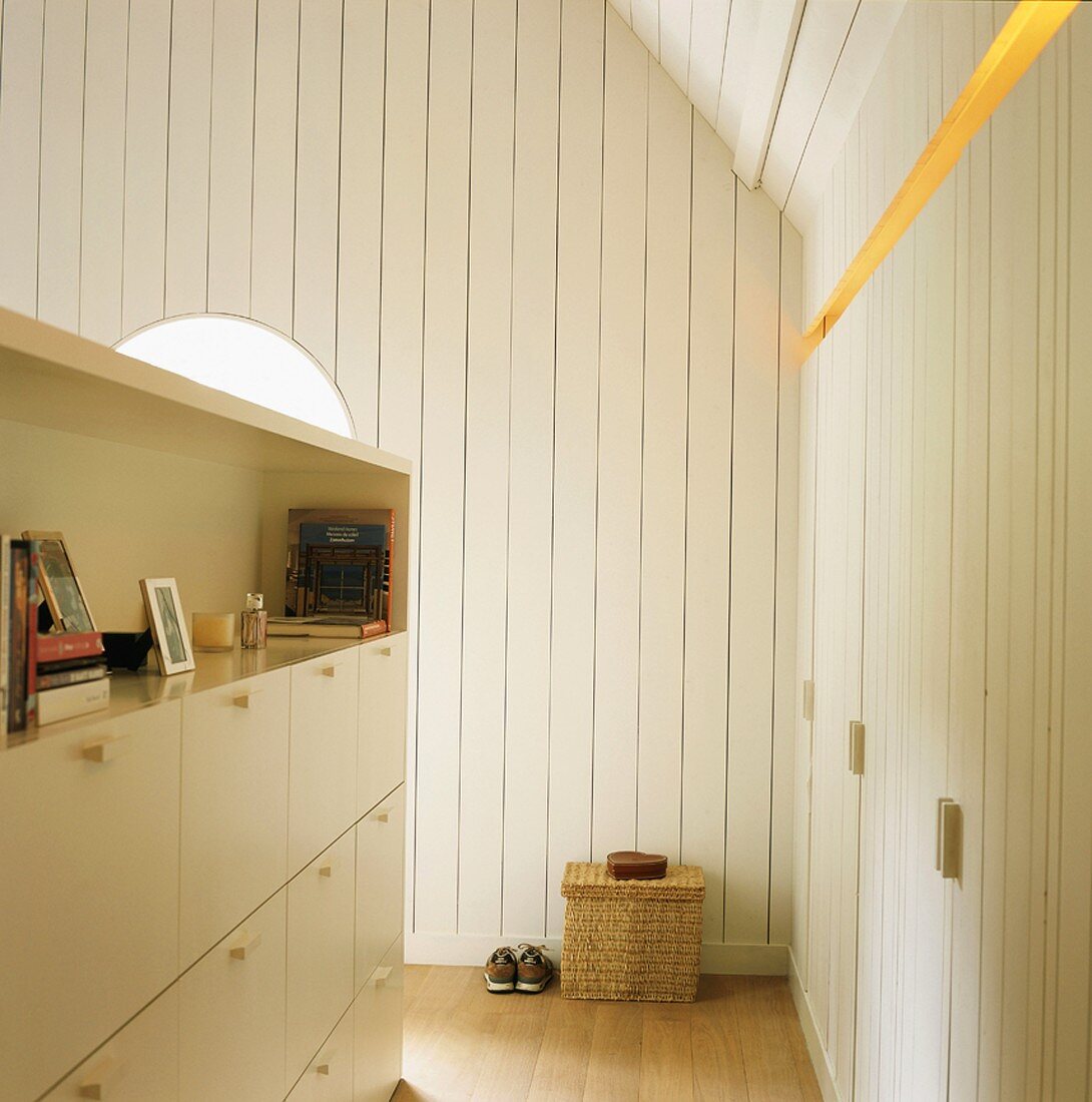 Converted attic with white wood panelling and half-height cabinet used as partition opposite custom fitted cupboards