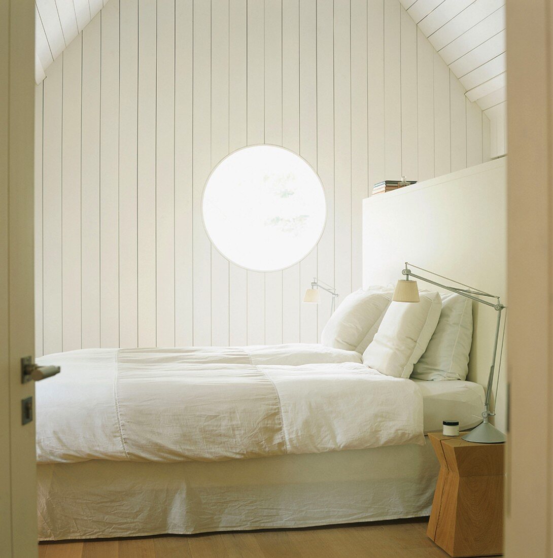 Double bed with white linen bedclothes in attic bedroom with white-painted, wood-clad walls