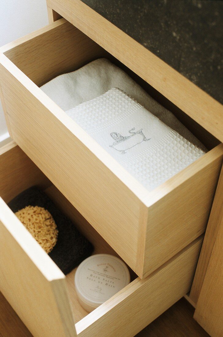 Geöffnete Holzschubladen mit weißen Handtüchern und Natur-Badeschwamm