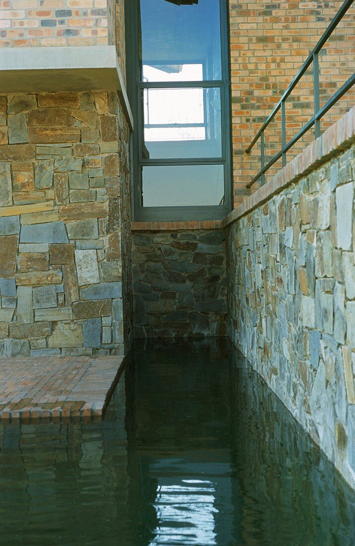 Wasserbecken im natursteinverkleideten Sockelbereich eines zeitgenössischen Hauses