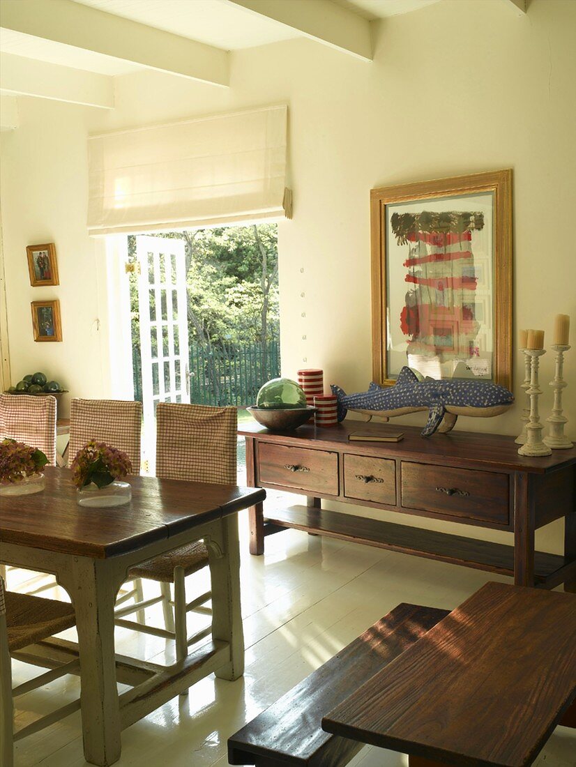 Dining room in rustic, country-house style with wall ornament on sideboard next to open French doors
