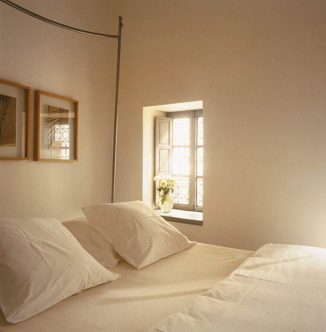 Kleine Fensternische mit innenliegenden Klappläden neben Doppelbett mit frischen, weissen Kissen