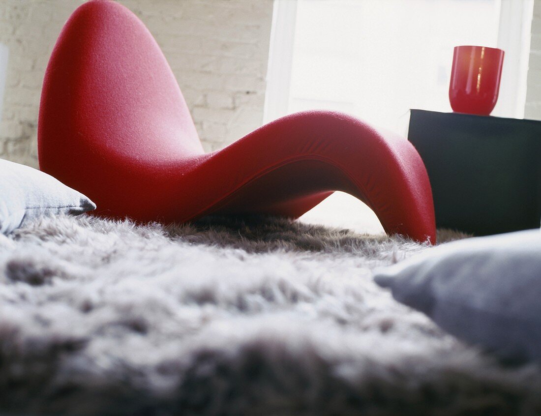 Knallrote Sitzliege auf Hochflor-Teppich und roter Becher auf Beistelltisch