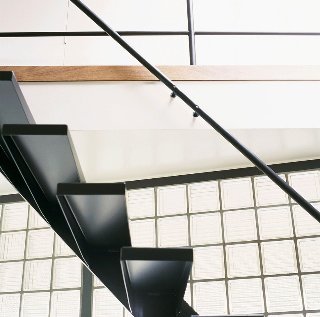 Untersicht schwarzer Treppenstufen aus Stahl mit Geländerstange vor Glasbausteinen