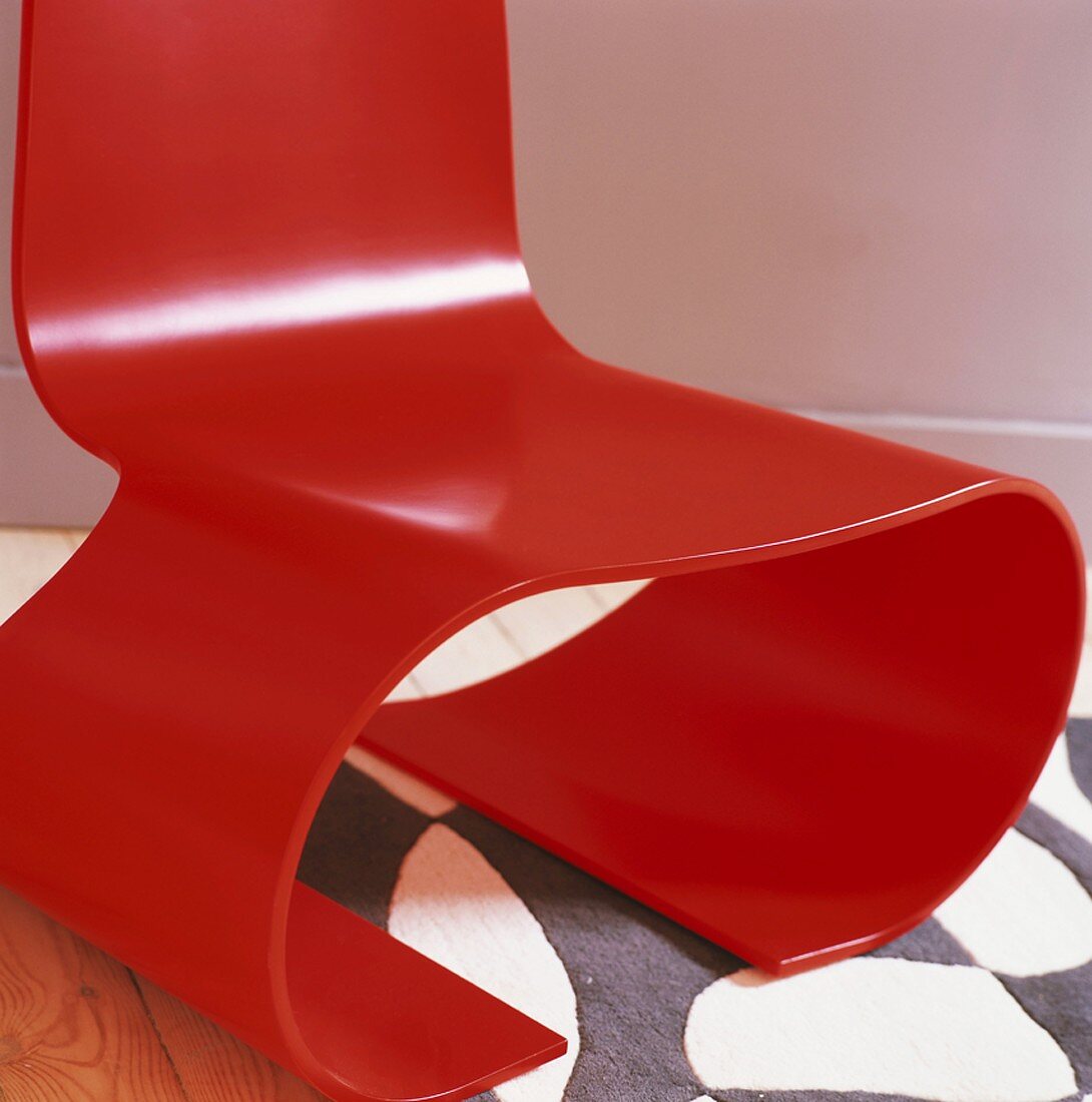 Roter Designer-Stuhl aus gebogenem Schichtholz auf modern gemustertem Teppich