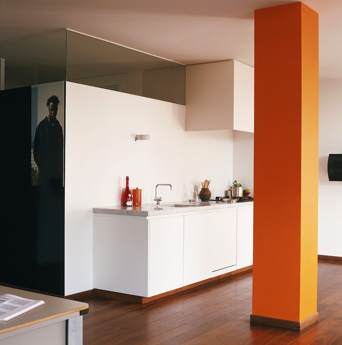 Open-plan interior with white kitchen counter and orange column