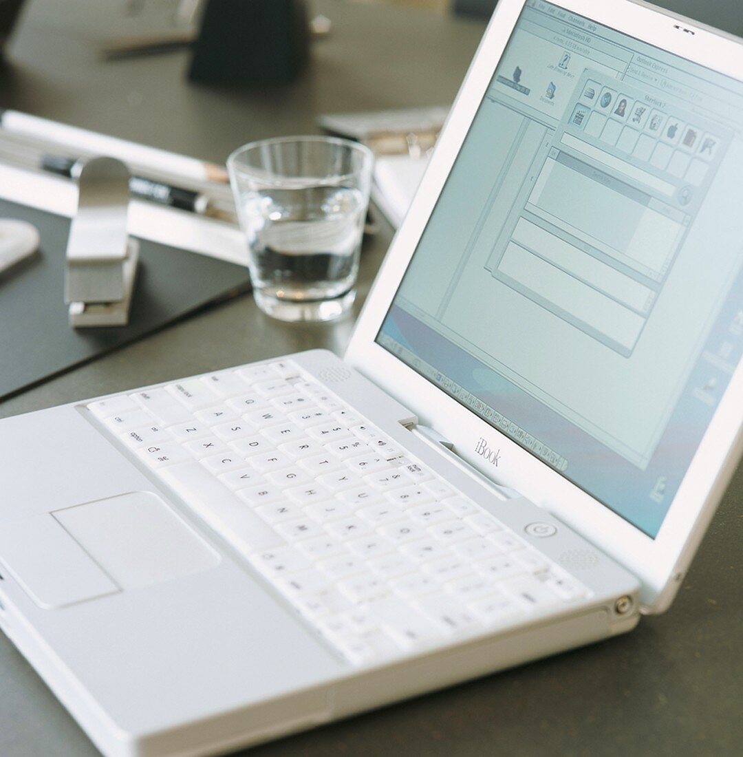 Aufgeklappter, weisser Laptop und Wasserglas auf einem Schreibtisch