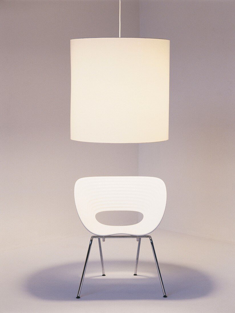 White shell chair with steel tube frame below large pendant lamp