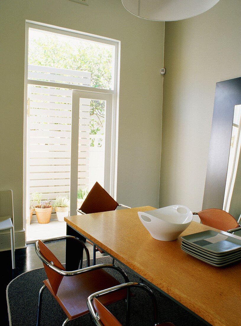 Stahlrohrstühle und Esstisch mit Porzellanschüssel und gemusterten Tellern vor dem offenen Terrassenausgang einer Wohnküche