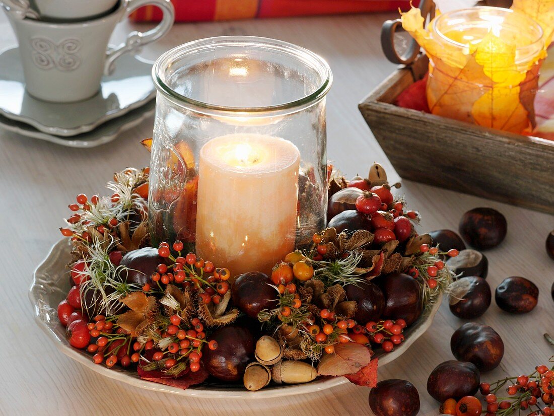 Candle in glass in wreath of rose hips, chestnuts and acorns