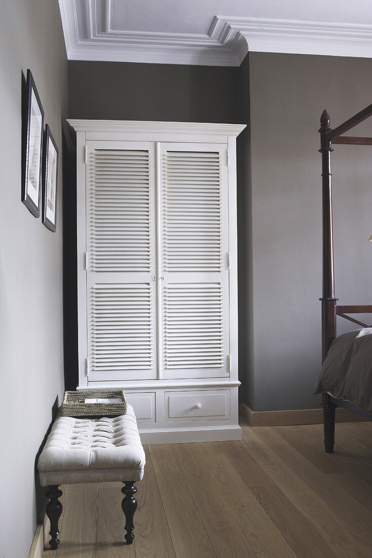 Traditional bedroom painted warm grey with elegant bedroom bench in front of country-house-style wardrobe