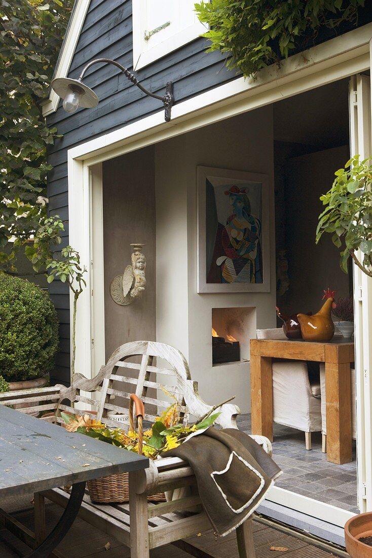 Terrace furnished in country-house style in front of wide terrace doorway leading to dining room in clapboard house