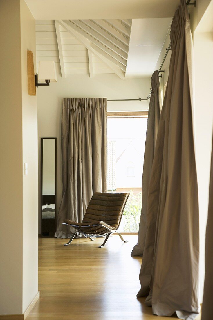 Bedroom with narrow full-length mirror, designer armchair and flowing curtains