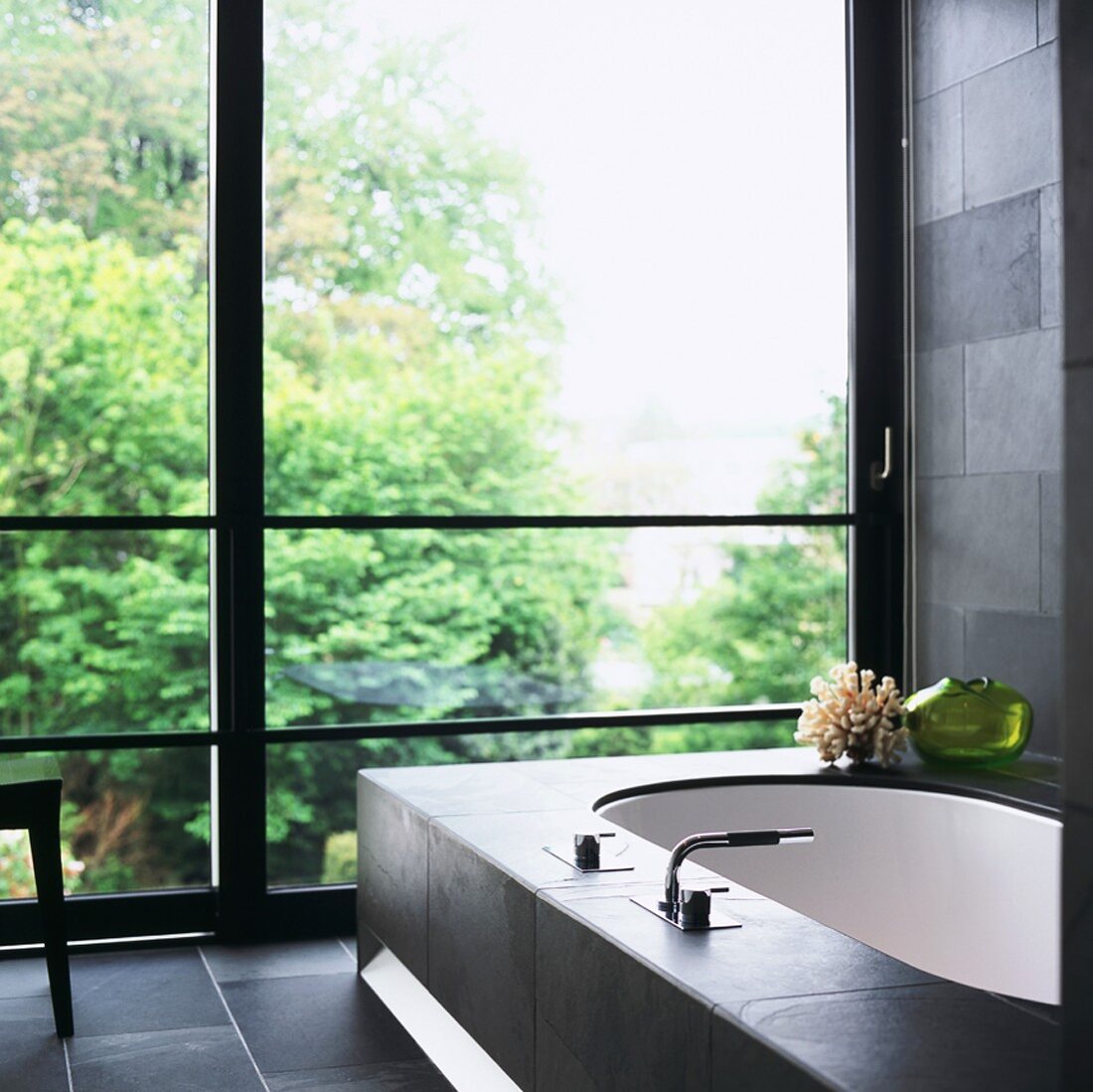 Modern bathroom with charcoal stone tiles and bathtub in front of glass wall