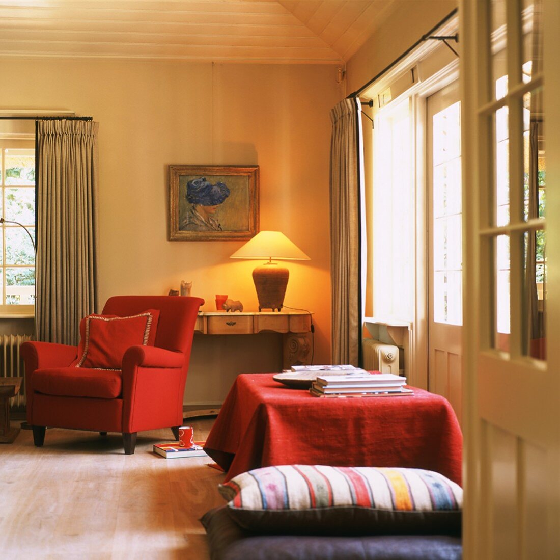 Cheerful interior with warm light from table lamp, red armchair and large floor cushions