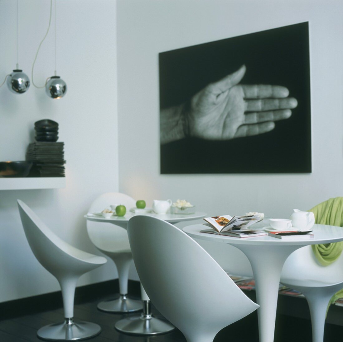 Corner of modern interior with white shell chairs, round table and black and white photo on wall