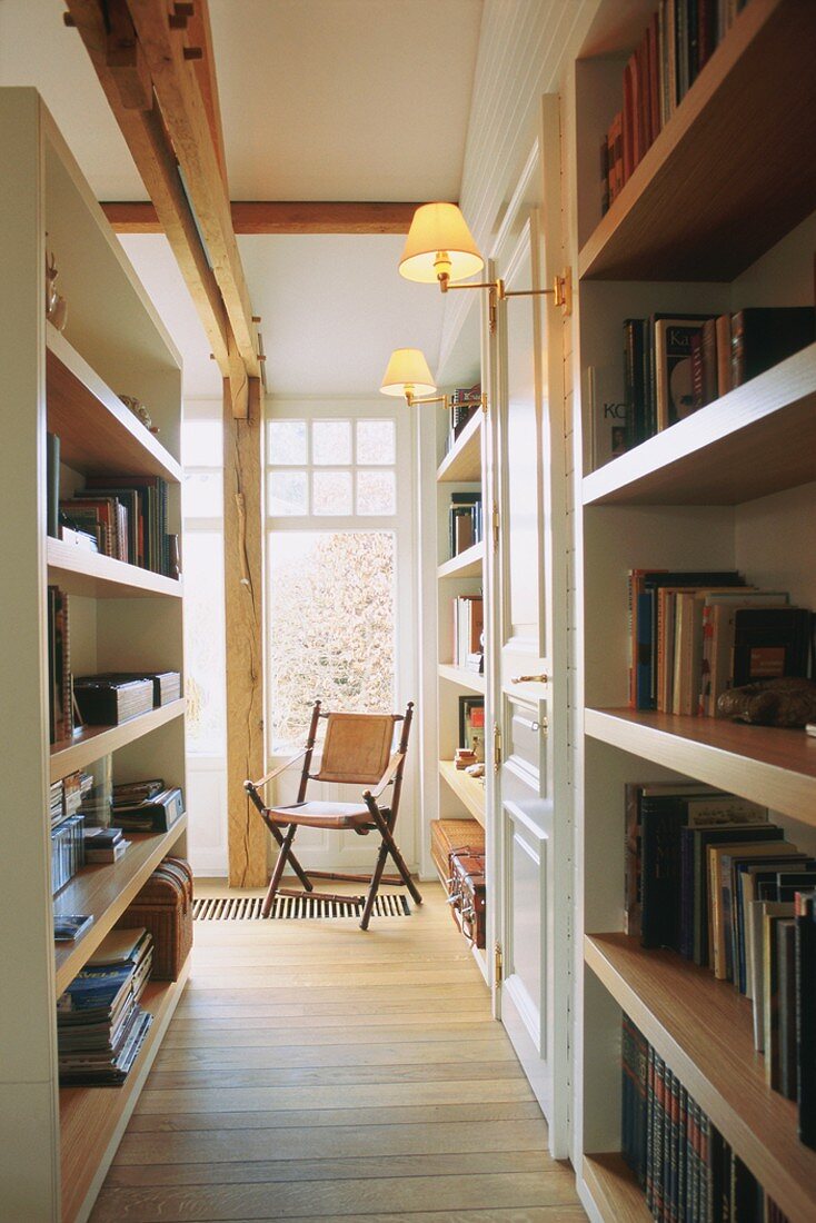 Flur mit Bücherwänden und Klappstuhl vor großem Fenster