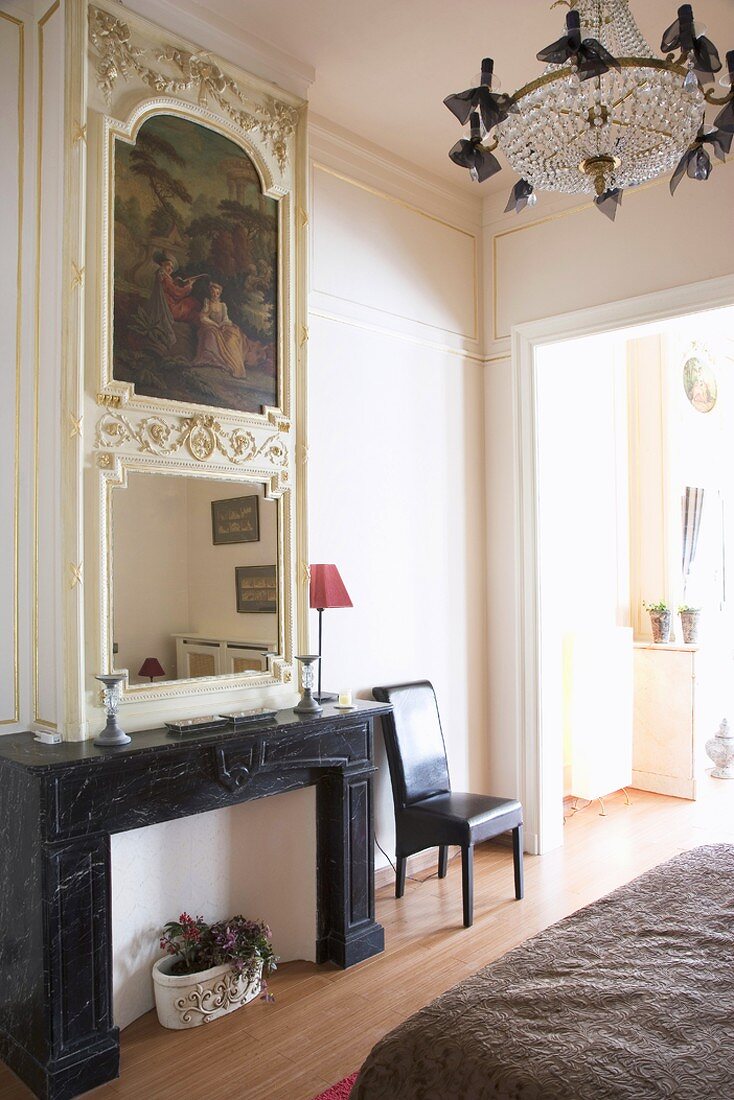 Disused open fireplace with built-in painting and mirror in bedroom with crystal chandelier