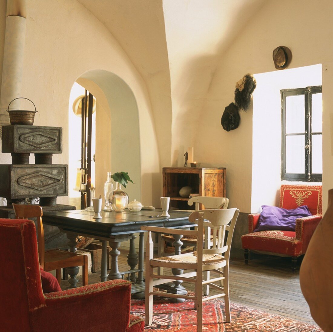 Living room with vaulted ceiling, wood-burner, arched open doorway, antique wooden table and armchairs with gold embroidery